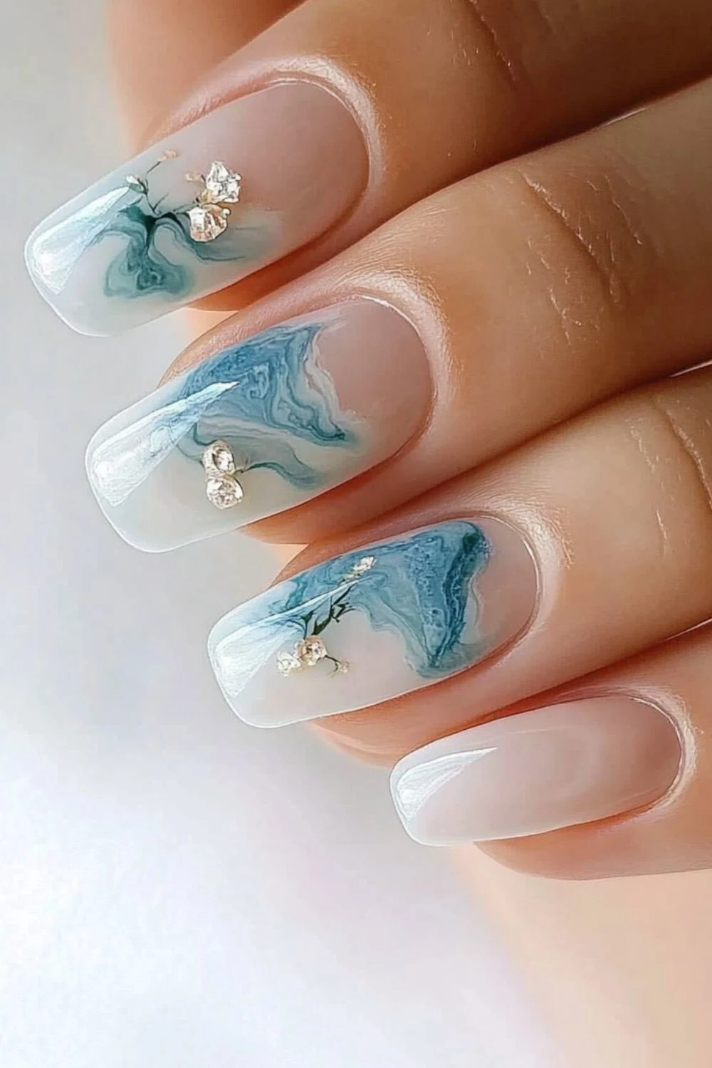 Elegant ocean marble nails with a translucent base, soft blue wave patterns, and delicate gold and gemstone accents.