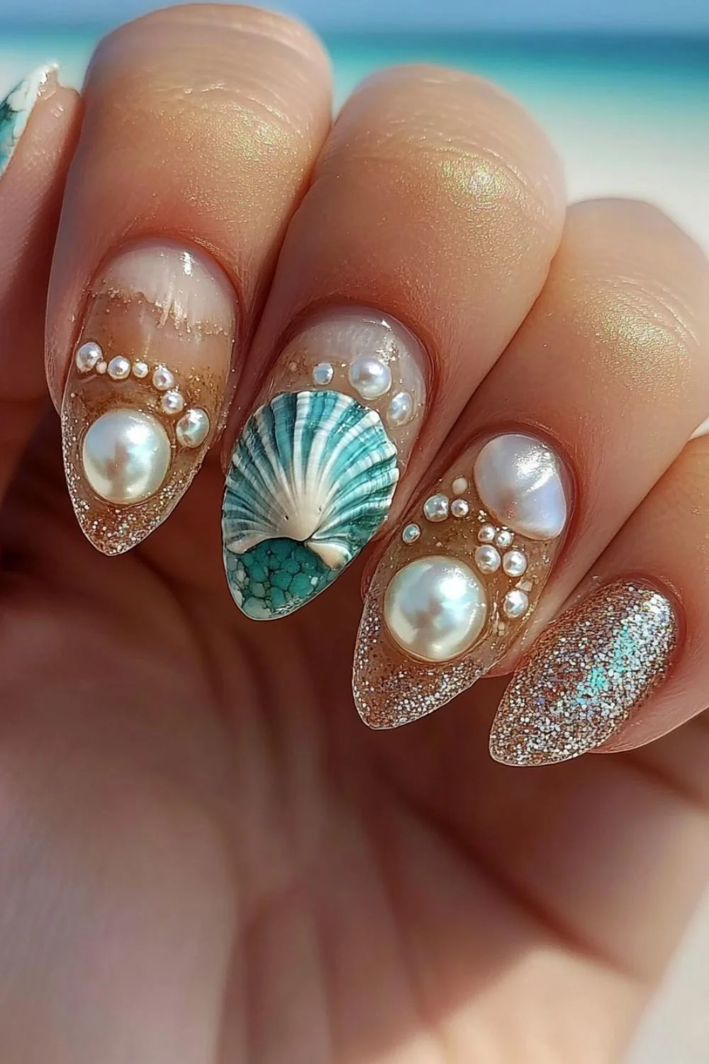 Transparent beach-inspired nails with pearl accents, a turquoise seashell design, and glittery sand-like details.