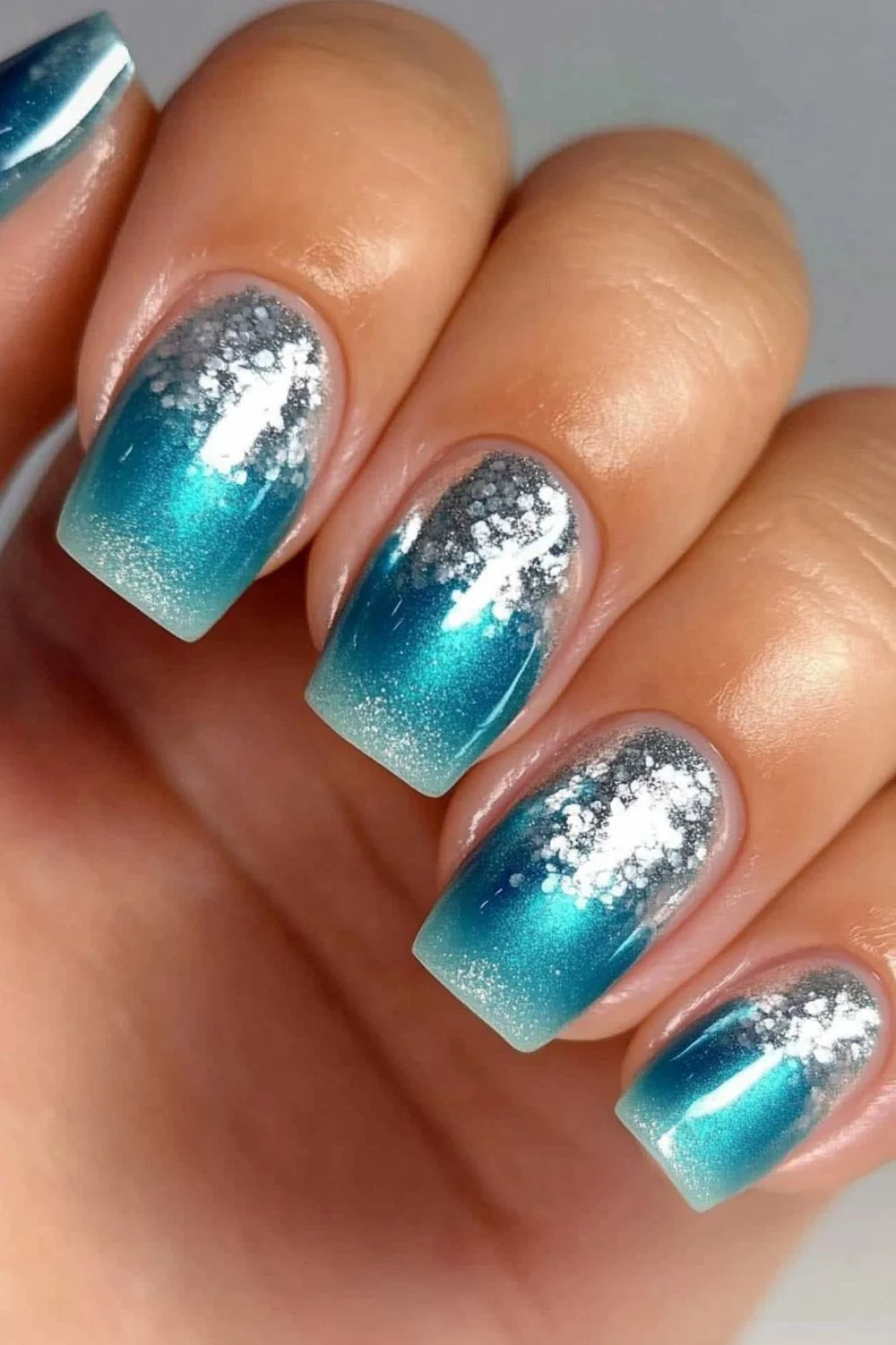 Square-shaped nails with a turquoise and silver glitter gradient, resembling sunlight reflecting on ocean waves.