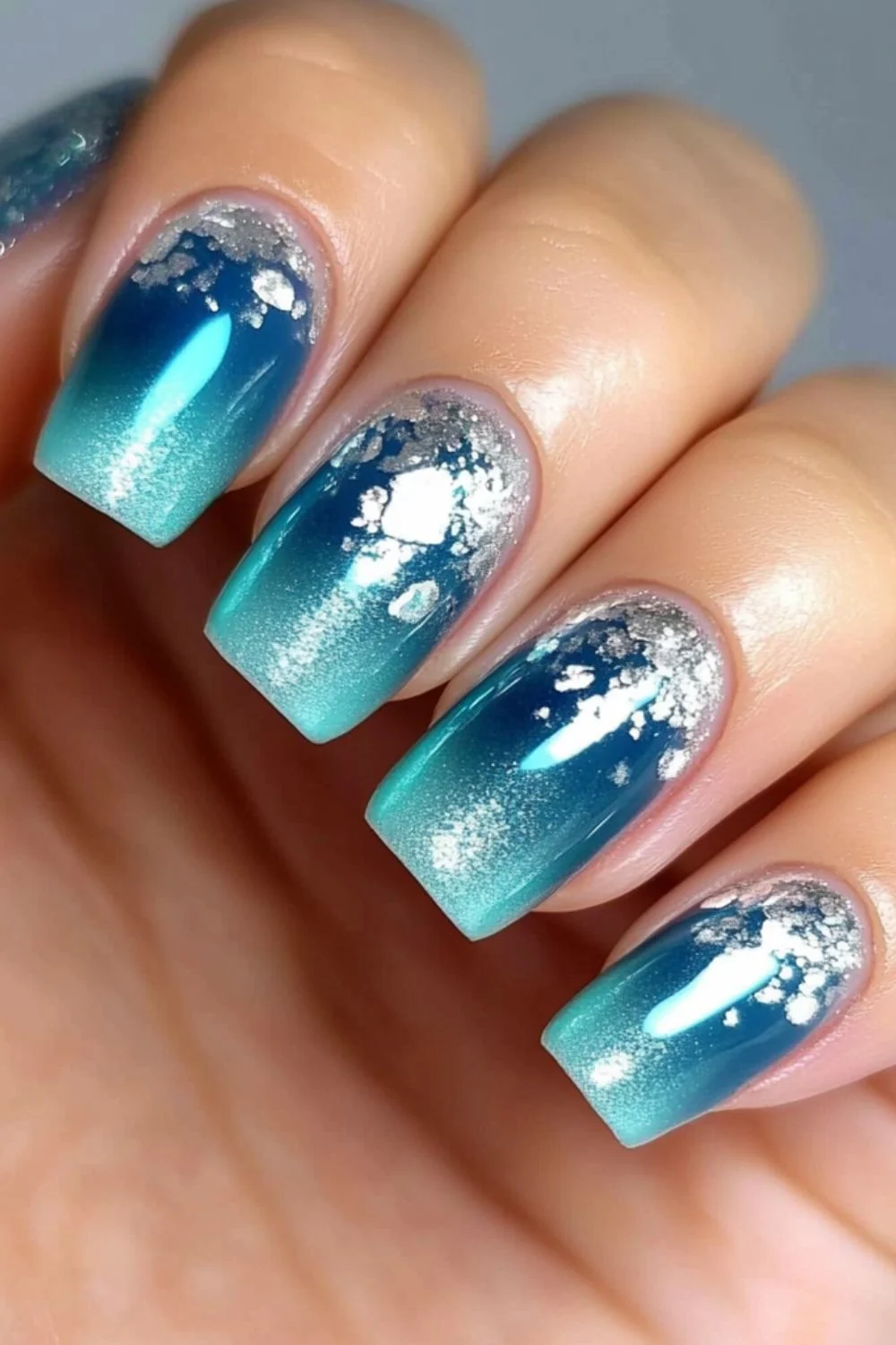 Square-shaped nails with a blue-to-teal gradient and silver foil accents, mimicking sunlight on ocean waves.