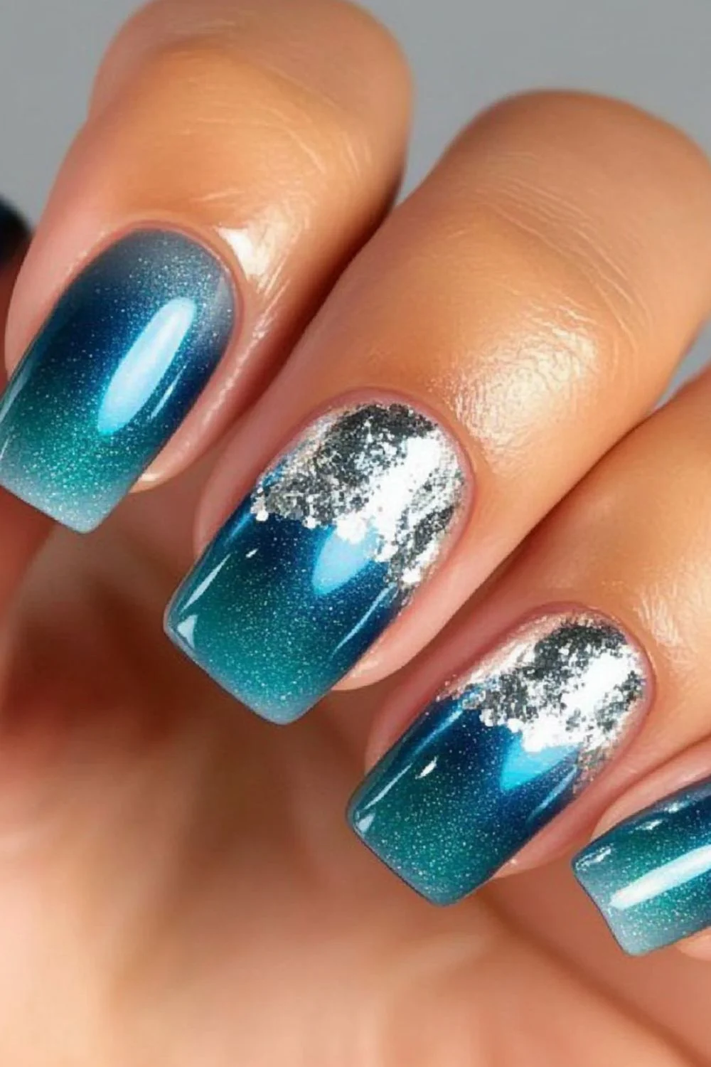 Square-shaped nails with a deep blue gradient and silver foil accents, mimicking crashing ocean waves.