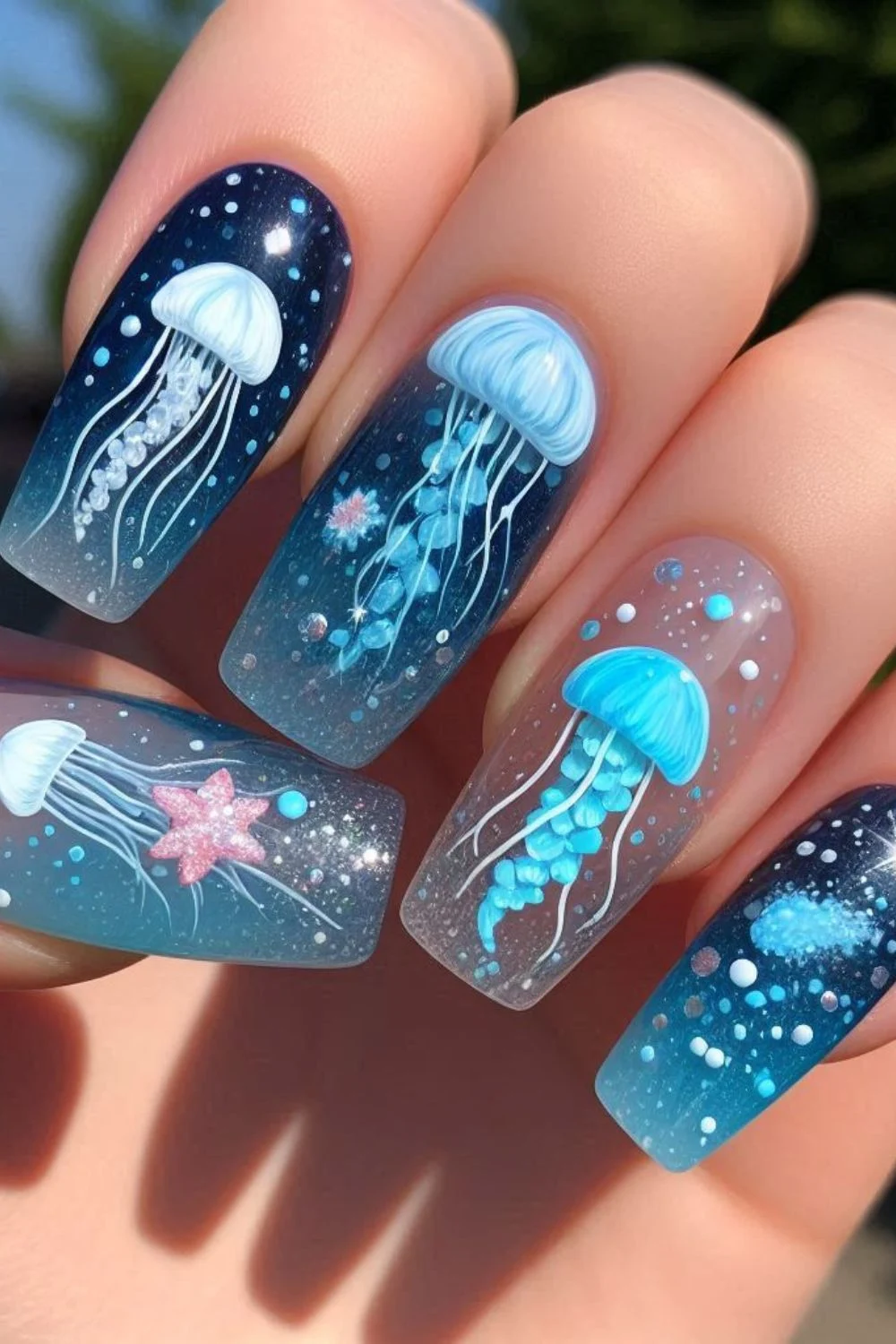 Square-shaped nails with a dark blue gradient, featuring hand-painted jellyfish, starfish, glitter, and underwater bubble accents.
