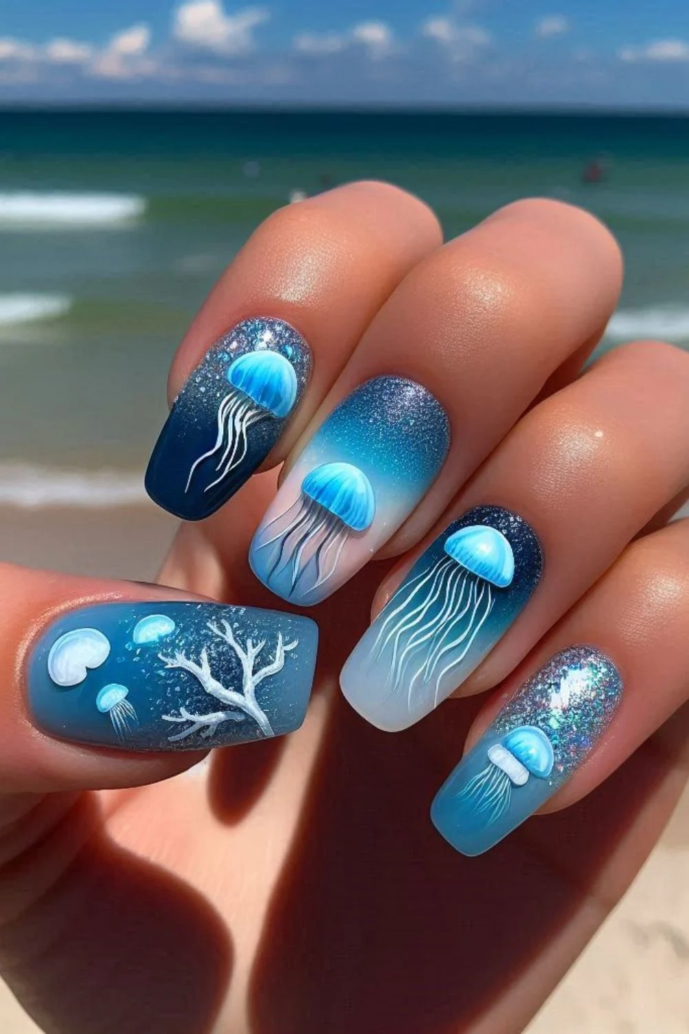 Square-shaped nails with hand-painted blue jellyfish, ocean gradients, glitter, and coral designs for a magical underwater-inspired manicure.