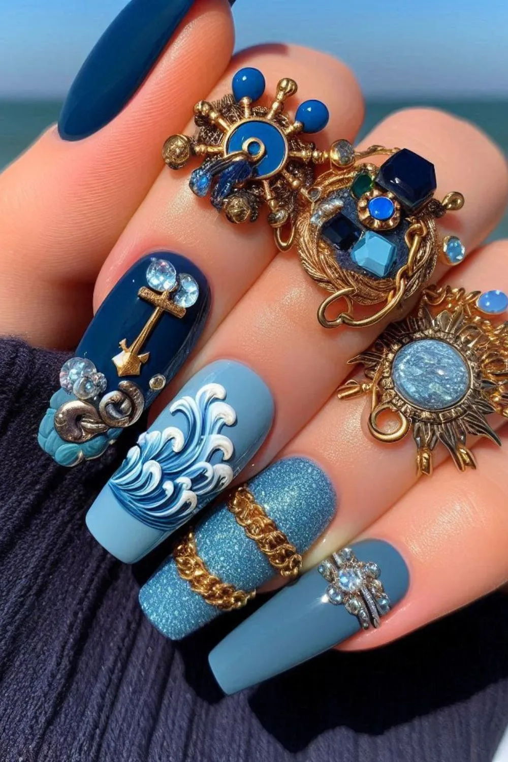 Long blue nails with gold chains, anchor embellishments, and 3D wave designs for a glamorous nautical-inspired manicure.