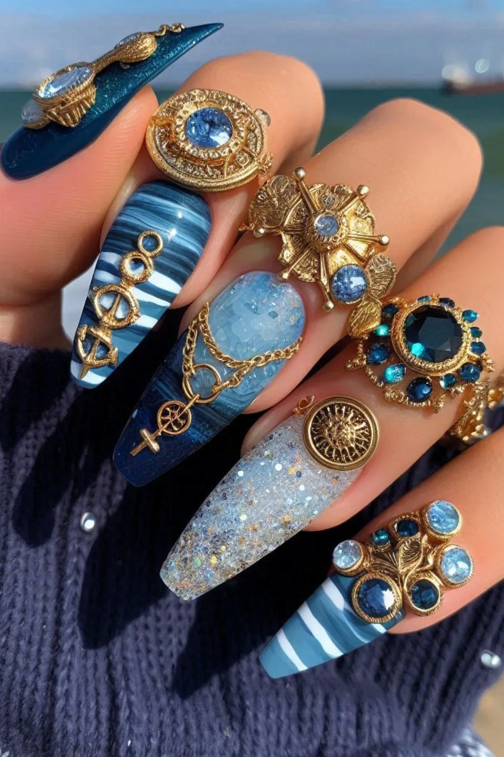 Deep blue and white nails with gold nautical embellishments, chains, and gemstone accents for a luxurious ocean-inspired manicure.