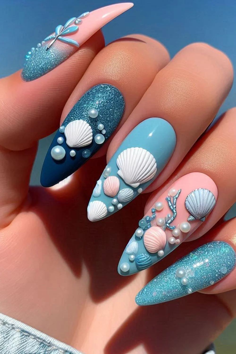 A close-up of ocean-themed nails decorated with seashells, pearls, and sparkling blue polish, creating a dreamy underwater effect.