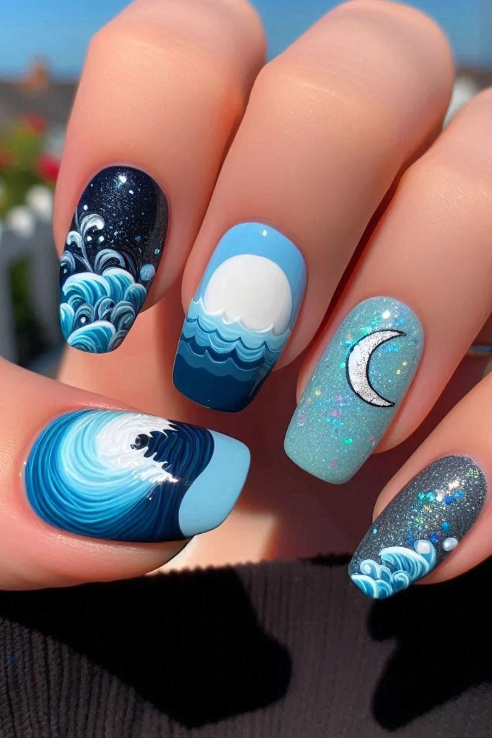 A set of long, coffin-shaped nails with a moonlit ocean theme. The nails feature hand-painted waves, a glowing full moon over the sea, a shimmering crescent moon, and glittery night sky accents, creating a celestial ocean-inspired look.