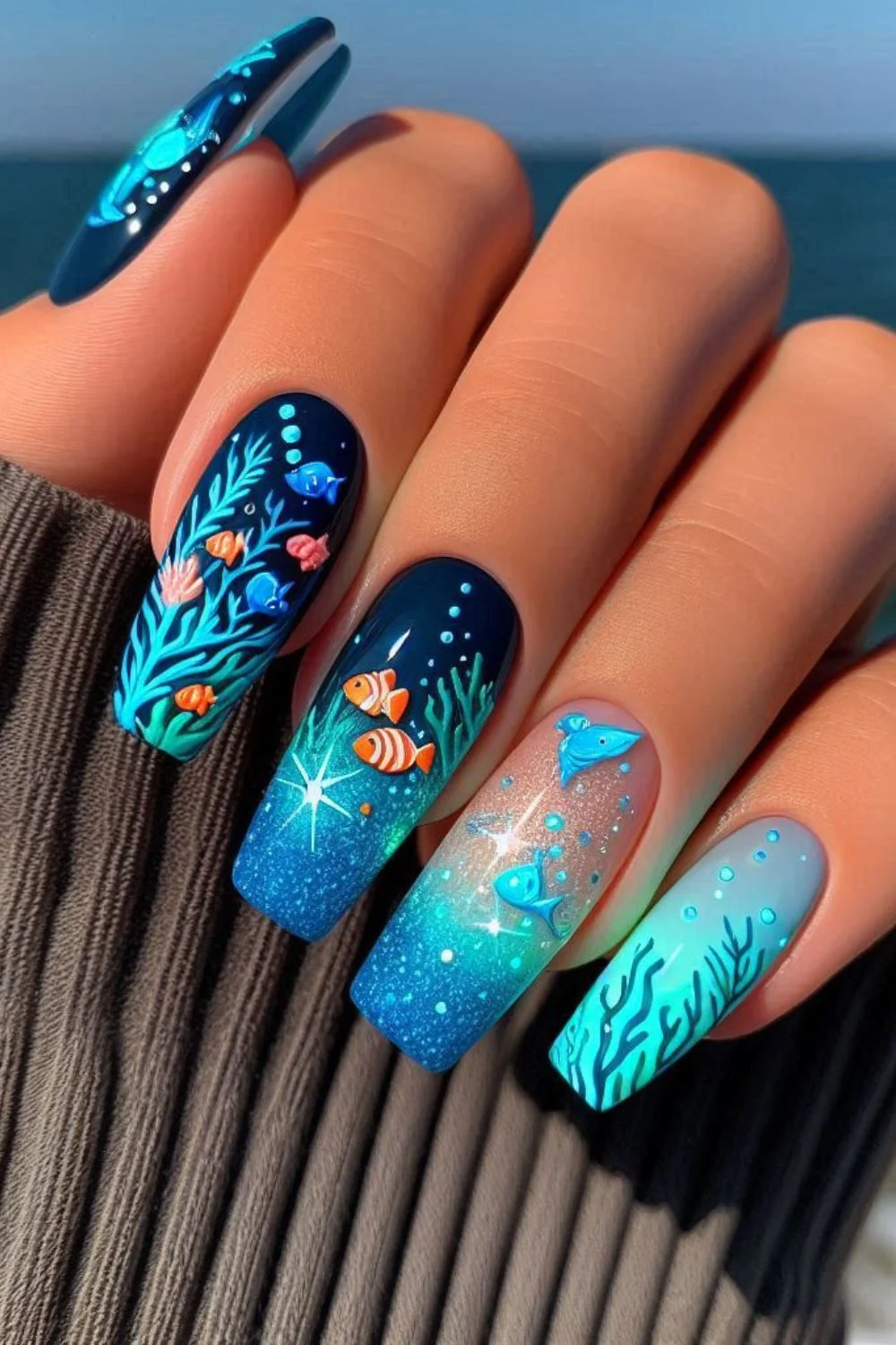 A set of long, coffin-shaped nails with an ocean-inspired design. The nails feature a gradient from deep navy blue to bright turquoise, decorated with hand-painted coral, fish, bubbles, and glowing jellyfish, creating an underwater scene.