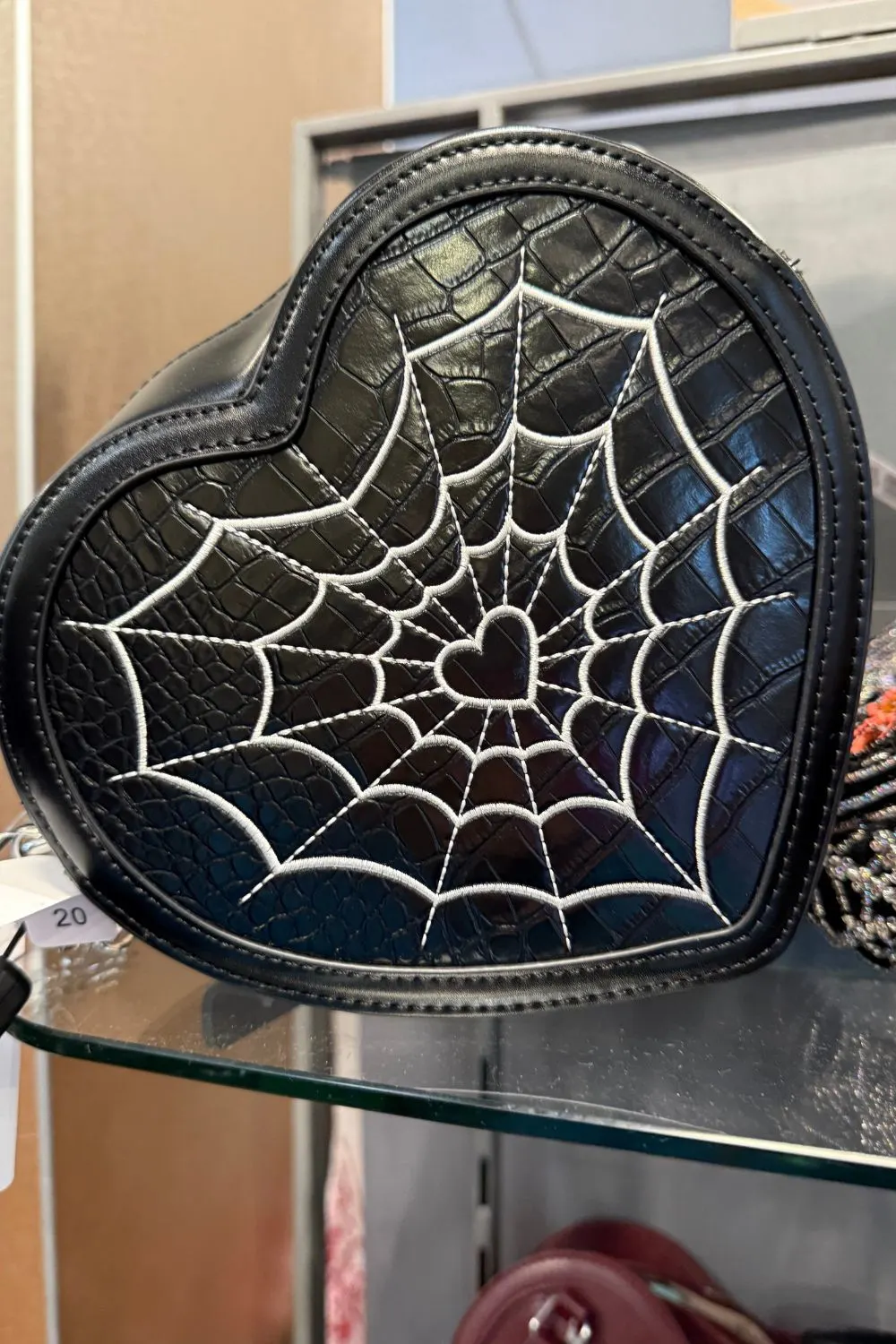Black heart-shaped handbag with a white embroidered spiderweb and heart detail in the center.