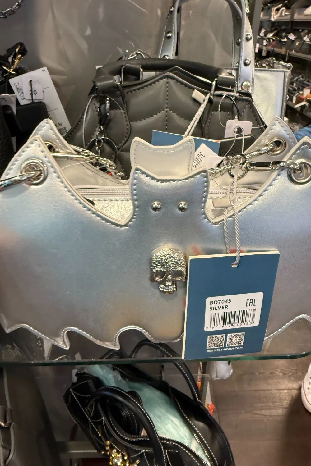 Silver bat-shaped handbag with a small metallic skull in the center.