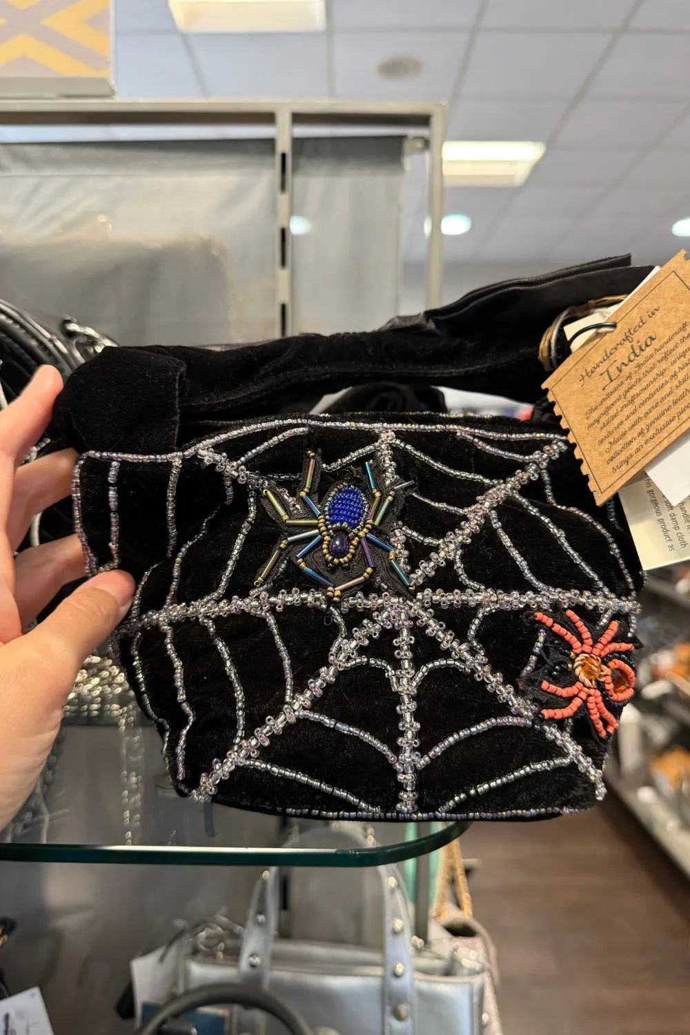 Black handbag decorated with silver beaded spiderwebs and two colorful beaded spiders.
